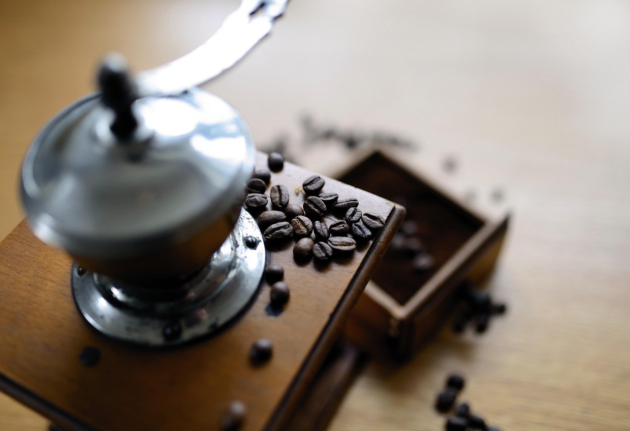 Alat penggiling kopi manual dengan hasil gilingan biji kopi yang tersebar di atas meja kayu