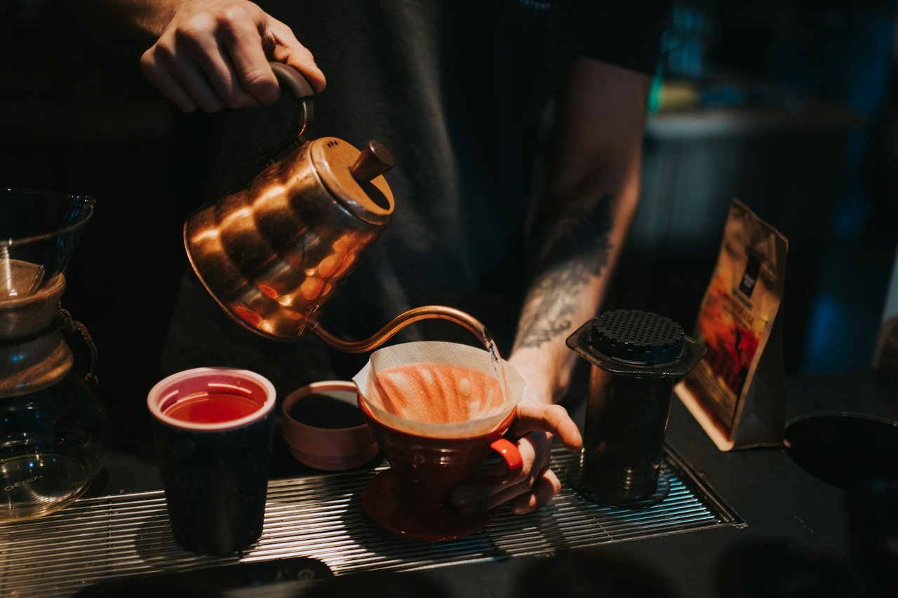 Barista menuangkan air panas secara melingkar perlahan dari teko leher angsa ke atas dripper V60