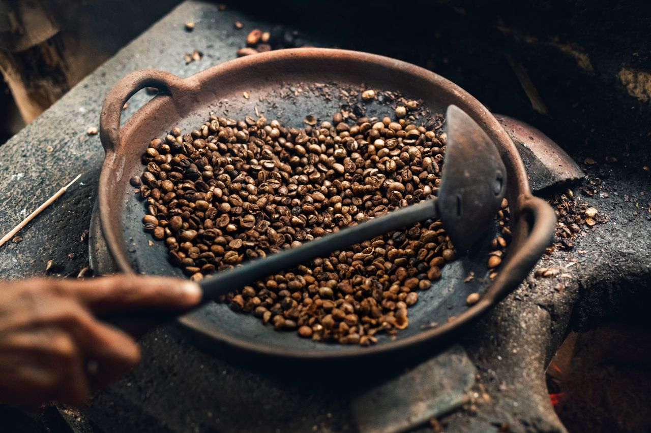 Biji kopi disangrai di atas wajan bulat dengan api tradisional